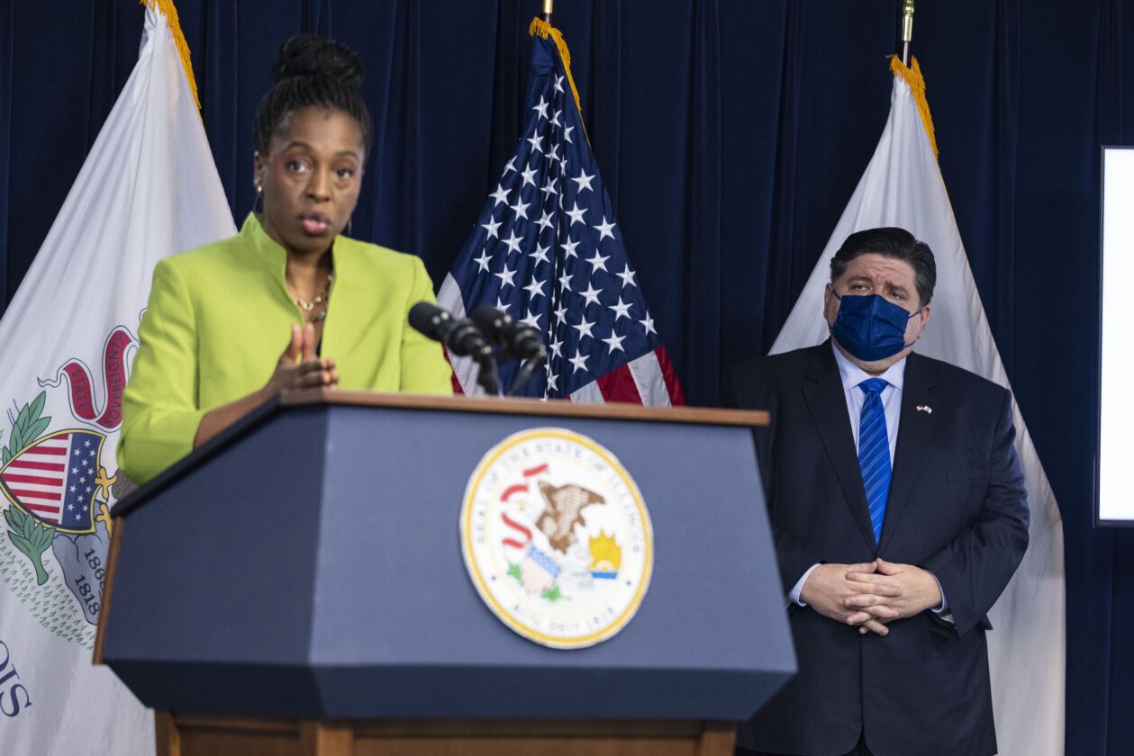 Gov. J.B. Pritzker listens as Dr. Ngozi Ezike briefs the media at the James R. Thompson Center in the Loop in May.